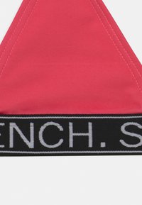 Rotes Dreieck-Bralette mit schwarzem Gummiband, auf dem weißer Text zu sehen ist. Es hat saubere Nähte und eine glatte Textur.