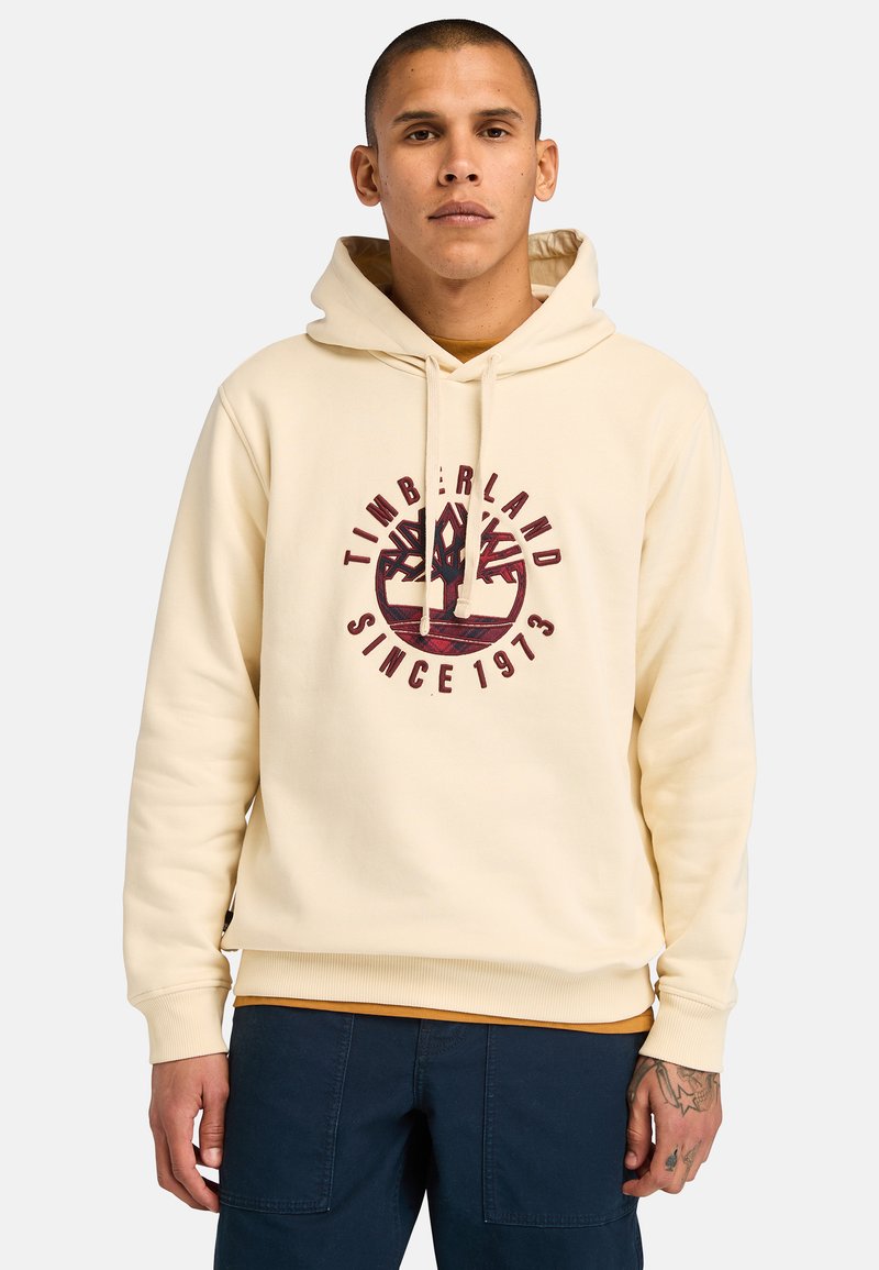 Felpa crema con cappuccio e cordoncino, caratterizzata da un logo Timberland bordeaux e dalla scritta "SINCE 1973" in un design circolare. Tessuto morbido, polsini a coste.