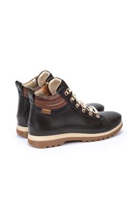 Botas de tobillo de cuero en negro con detalles en marrón, que presentan cordones con herrajes dorados, un collar acolchado y una suela de goma texturizada.