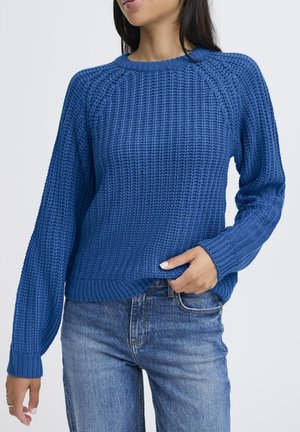 Blauer, gestrickter Pullover mit strukturiertem Muster, Rundhalsausschnitt und langen Ärmeln, kombiniert mit hellblauen Jeans.