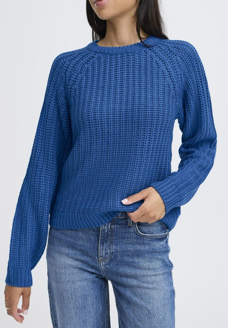 Pull en laine bleu avec un motif texturé, col rond et manches longues, associé avec un jean bleu clair.