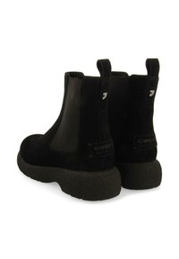 Botas de tobillo de ante negro con paneles laterales elásticos y suelas de goma texturizada negra. Presenta un parche con el logo en la parte trasera.