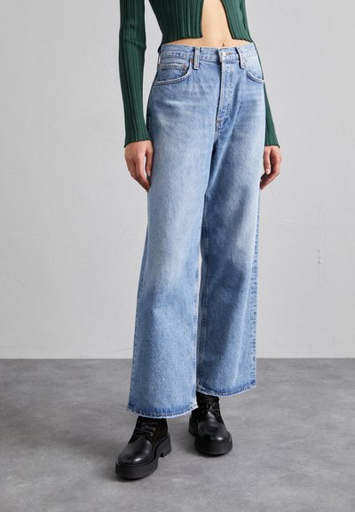 Φωτεινά μπλε τζιν σε γραμμή wide-leg, κατασκευασμένα από τζιν ύφασμα, με ψηλή μέση, φραγμένο στρίφωμα και διακριτικές λεπτομέρειες ραφής. Φοριούνται με μαύρες μποτάκια με κορδόνια.