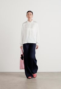 Blouse blanche à manches longues avec col, pantalon large en denim sombre, sac tote rose et chaussures roses assorties à enfiler. Design minimaliste.