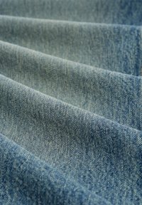 Denim tkanina u svijetloplavoj boji, s izraženim twill uzorkom i suptilnom teksturom, s valovima koji ukazuju na nabore i drapiranje.