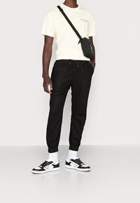 Zwarte linnen joggers met elastische boorden, gecombineerd met een gele t-shirt. Een zwarte schoudertas en zwart-witte sneakers maken de look compleet.