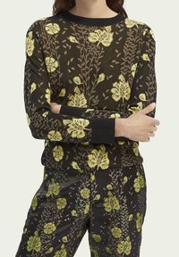 Jersey de punto con base negra y patrón floral amarillo, que cuenta con mangas largas y puños acanalados. Textura suave con un diseño ajustado.