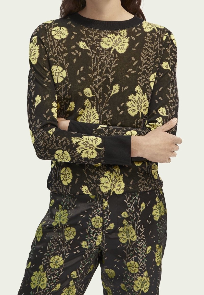 Jersey de punto con base negra y patrón floral amarillo, que cuenta con mangas largas y puños acanalados. Textura suave con un diseño ajustado.