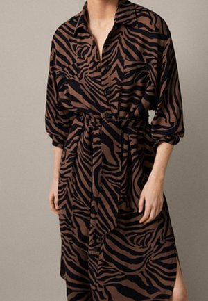 Woman wearing a brown and black zebra-print belted shirt dress with 3/4 sleeves against a plain background.