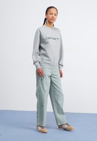 Grå sweatshirt med "carhartt" logo, stribede lysegrønne bukser og beige sko med hvide detaljer. Enkel, funktionel design, afslappet pasform.