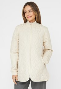 Quilted cream jacket with a stand-up collar, front zipper, and two pockets. Features ribbed cuffs and curved hem. Smooth texture.