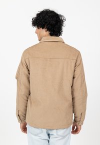 Khaki kurtka z korduroy z szpiczastym kołnierzem, zapinana na guziki, z mankietami i karczkiem na plecach. Posiada miękką, teksturowaną powierzchnię oraz luźny krój.