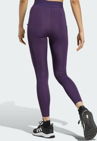 Ljubičaste tajice visokog struka s bočnim džepovima, izrađene od rastezljivog materijala. Uparene s crnim sportskim tenisicama s bijelim detaljima.