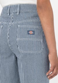 Modré a bílé pruhované kalhoty vyrobené z odolné látky, s zadní kapsou s červeným a žlutým logem "Dickies".