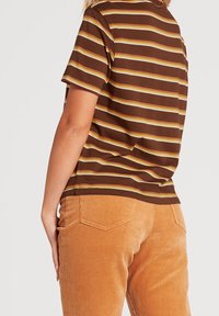 Chemise à manches courtes rayée marron associée à un pantalon en velours côtelé marron clair, avec des côtes verticales et des poches arrière.