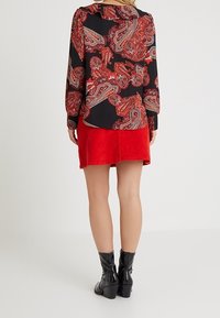 Svart blus med röd paisleymönster, som matchas med en röd corduroy kjol och svarta lackade ankelstövlar med tjocka klackar.