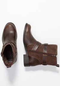 Botines marrones con un upper de cuero liso, un cierre lateral y un acabado de ante texturizado. Tacón bloque resistente con detalles de correa ajustable.
