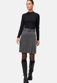 Haut à manches longues noir, jupe plissée grise à motifs avec une ceinture, bottes noires montantes avec une petite boucle en accent. Texture lisse.