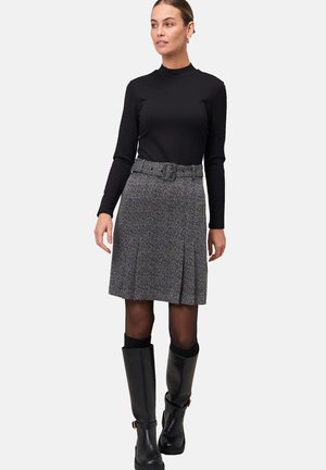 Haut à manches longues noir, jupe plissée grise à motifs avec une ceinture, bottes noires montantes avec une petite boucle en accent. Texture lisse.