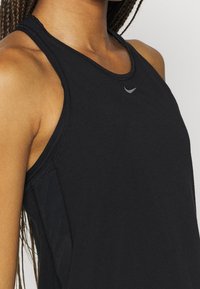 Närbild av en person som bär en svart ärmlös sporttopp med en liten reflektiv logotyp på bröstet.