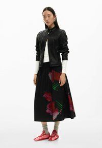 Mustast nahast jope, millel on liibuv lõige, kantud koos pika musta seelikuga, millel on värvikad abstraktsed mustrid, ning erksate punaste tossudega.