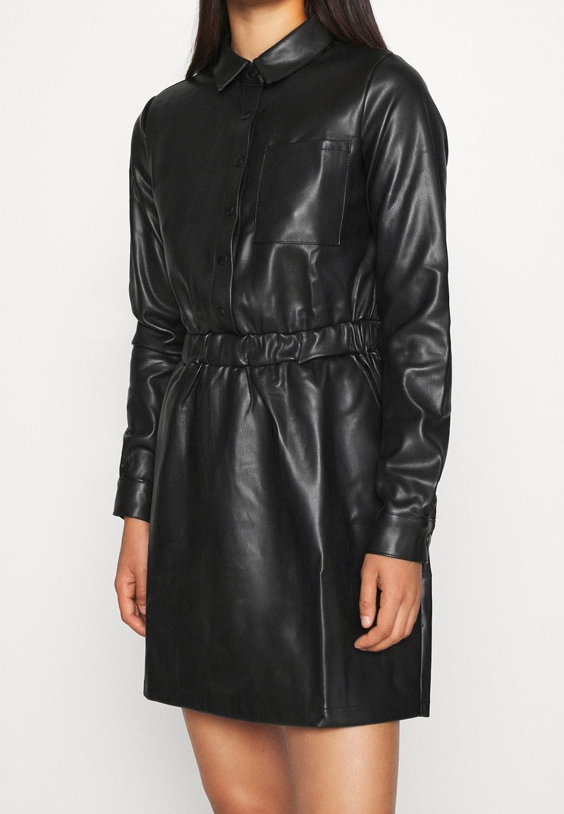 Svart läderklänning med krage, knappstängning, långa ärmar, framficka och elastisk midja för form. Slät textur genom hela plagget.