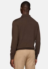 Suéter marrón de punto con un corte relajado, que presenta una textura acanalada y mangas largas. Combinado con pantalones beige de corte slim.