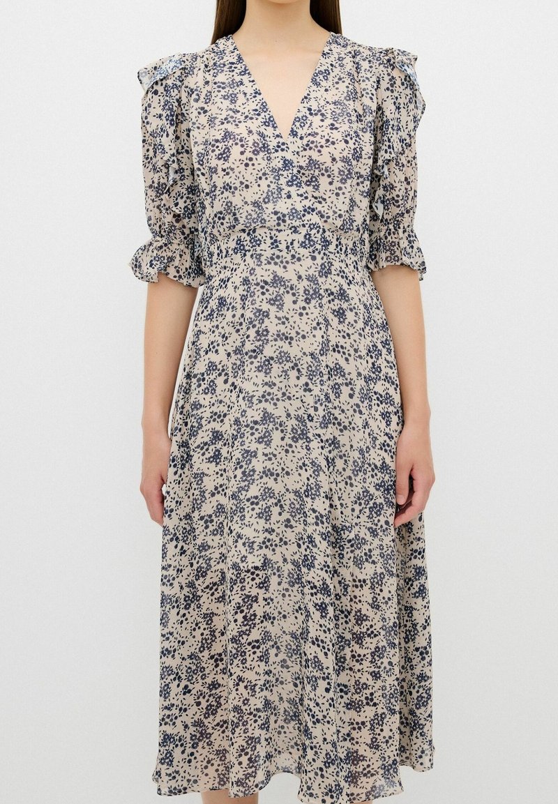 Robe midi fleurie en tissu léger, avec un décolleté en V, des manches à volants et une taille cintrée, sur un fond beige avec un imprimé marine.