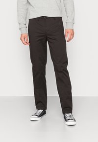 Dark brown cotton trousers with a straight fit, featuring a button closure and side pockets, paired with black and white sneakers.
