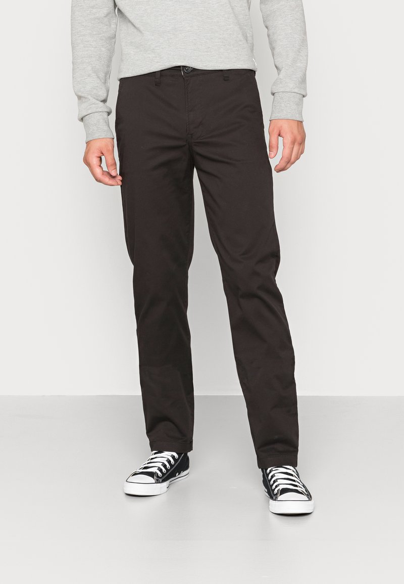 Dark brown cotton trousers with a straight fit, featuring a button closure and side pockets, paired with black and white sneakers.