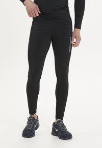 Svart sportleggings i elastiskt material, med sidofickor och reflektande detaljer. Matchas med marinblå löparskor.