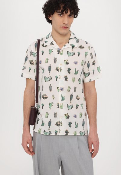 Camisa de manga corta, abotonada, en tejido ligero, con un estampado multicolor de cactus y plantas sobre un fondo crema. Combinada con pantalones gris claro.