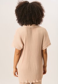 Pale pink, ribbed blouse with short sleeves and a collar; loose fit with a scalloped hemline, soft texture. Viewed from the back.