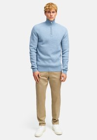 Jasnoniebieski sweter w prążki z kołnierzem na ćwierć zamek, zestawiony z beżowymi chinosami i białymi trampkami, prezentujący dopasowany krój i teksturowany materiał.