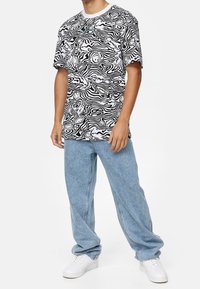 Černo-bílý tričko s abstraktním vzorem a kulatým výstřhem, v kombinaci s světle modrými volnými džíny a bílými teniskami.