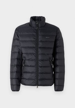 Giacca nera imbottita con colletto alto, caratterizzata da cuciture orizzontali, tasche con zip e un logo sul lato sinistro del petto. Materiale leggero.