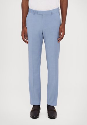 Lichtblauwe formele broek van glad materiaal, met een rechte snit, riemlussen en zijzakken, gecombineerd met donkere schoenen.