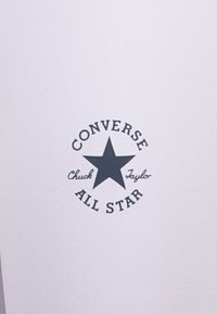 Converse All Star-logoet med en mørk stjerne og tekst i sirkelformat, plassert mot en lys, teksturert bakgrunn.