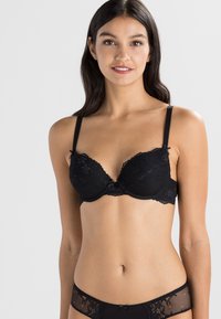 Zwarte kant beha met padded cups, verstelbare banden, bloemenpatroon en lichte padding. Gladde textuur en contrasterende accenten zijn aanwezig.