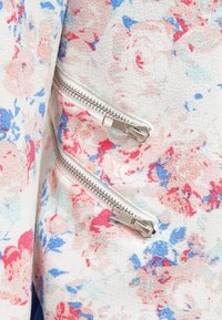 Gros plan sur deux tirettes de fermeture éclair argentées sur un tissu blanc à motif floral rouge, bleu et rose clair.