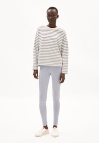 Gestreifter Langarm-Sweatshirt in Creme und Hellblau, kombiniert mit hellblauen Leggings und weißen Sneakern mit roten Akzenten. Einfaches Design.