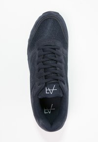 Mörkblå sneakers med en texturerad mesh-överdel och mockadetaljer, med en vadderad plös och platta snören. Logotypen är tydligt visad på plösen.