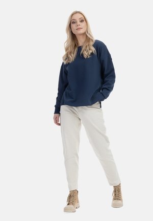 Navyblauwe sweatshirt met een relaxed fit, zijzakken en geribbelde manchetten, gecombineerd met crème-kleurige broeken en beige veterschoenen.