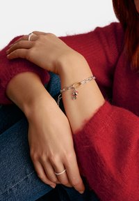 Silver chain bracelet with a gold accent and colorful charms, worn on a wrist against a backdrop of a red sweater and blue denim.