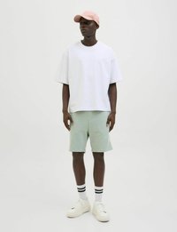 Witte oversized t-shirt, mintgroene shorts, roze pet, witte sneakers met dikke zool, en wit met zwarte gestreepte sokken. Eenvoudige, casual outfit.