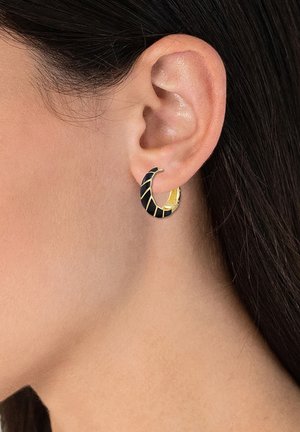 Boucle d'oreille noire et dorée en forme de spirale avec des couleurs alternées, mise en valeur sur une oreille contre une peau texturée.