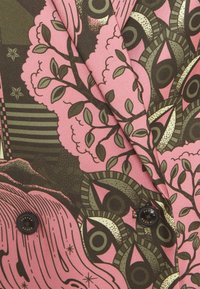 Tejido estampado que presenta diseños botánicos en tonos rosa y verde, con botones negros llamativos y formas abstractas. Material de mezcla de algodón texturizado.