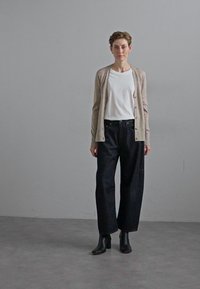 Beige cardigan over a white t-shirt, paired with loose black trousers and black ankle boots, set against a plain gray background.