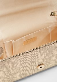 Złota torebka typu clutch z teksturą w wężowy wzór, z gładkim satynowym wnętrzem, z złotą plakietką z logo i bezpiecznym zapięciem na zatrzask.