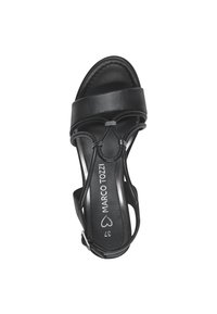 Black heeled sandal with smooth leather upper, thin straps, and a circular accent. Features a cushioned footbed and adjustable ankle strap.